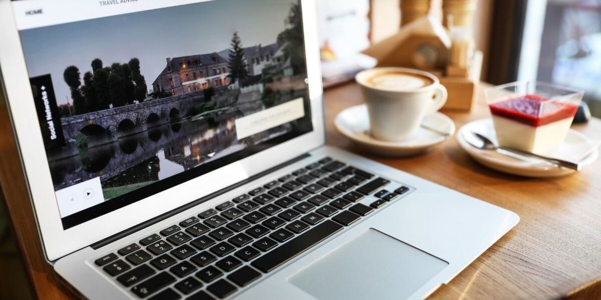 Blogger sitzt mit Notebook und dampfender Tasse Kaffee in Österreich im Cafe.