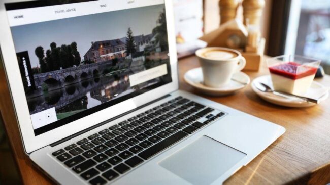 Blogger sitzt mit Notebook und dampfender Tasse Kaffee in Österreich im Cafe.
